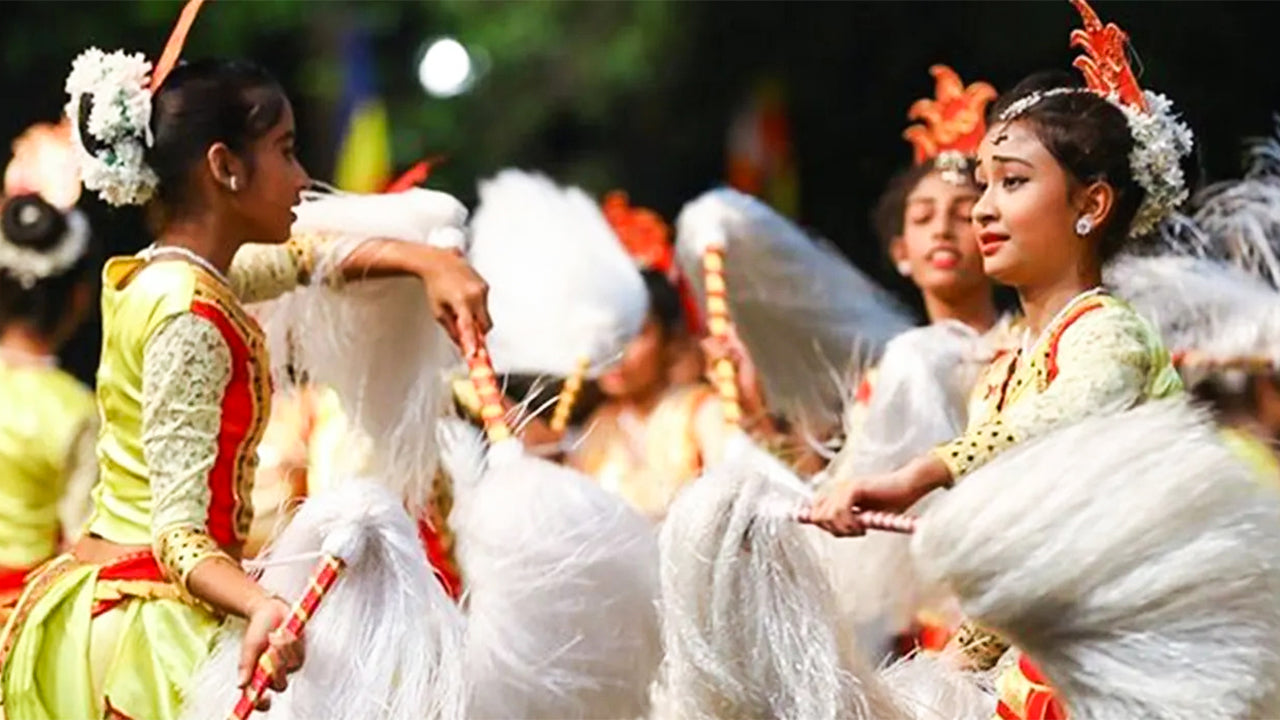 Traditional dancers participating in the Kandy Esala Perahera festival, dressed in colorful costumes and headdresses, performing with elephants in the background.