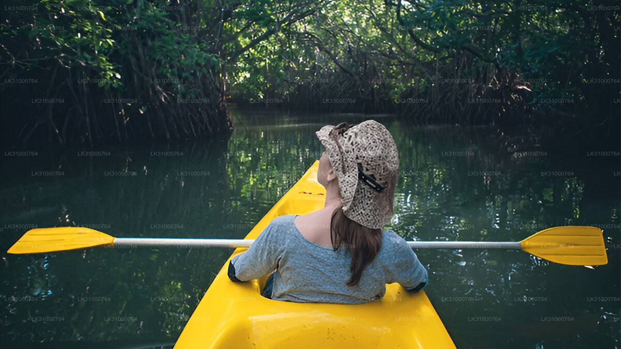 Person in a yellow kayak with a patterned hat on a calm waterway surrounded by greenery