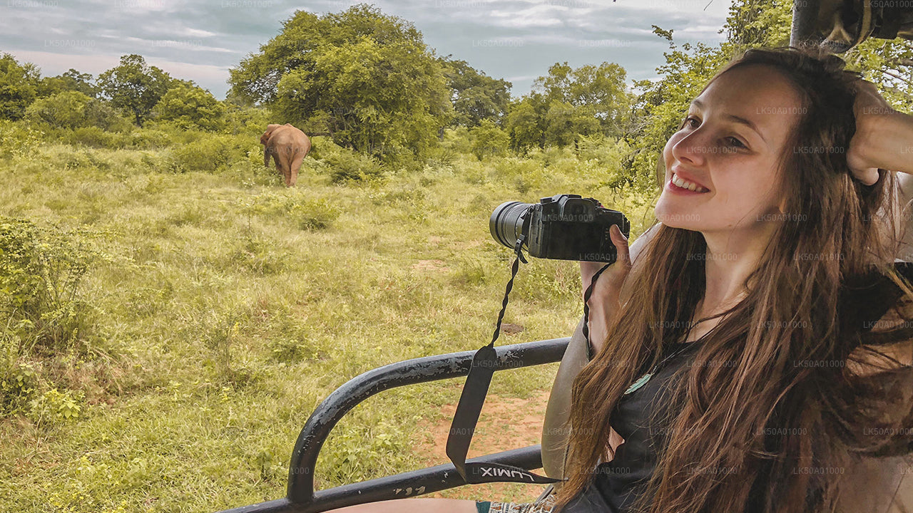 A person smiling while on a safari in Udawalawe National Park, with a elephant in the background.